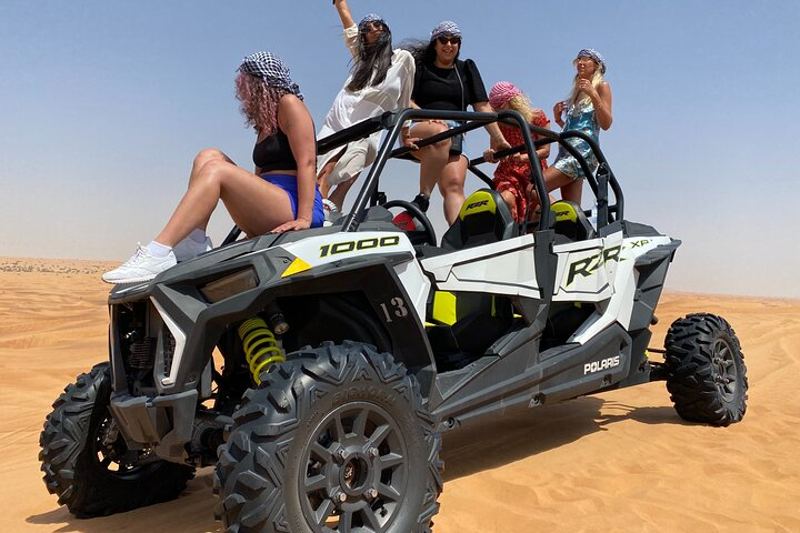 Experience the sprawling desert sands as you navigate thrilling trails in a dune buggy surrounded by friends laughter and a backdrop of golden dunes under a striking blue sky.